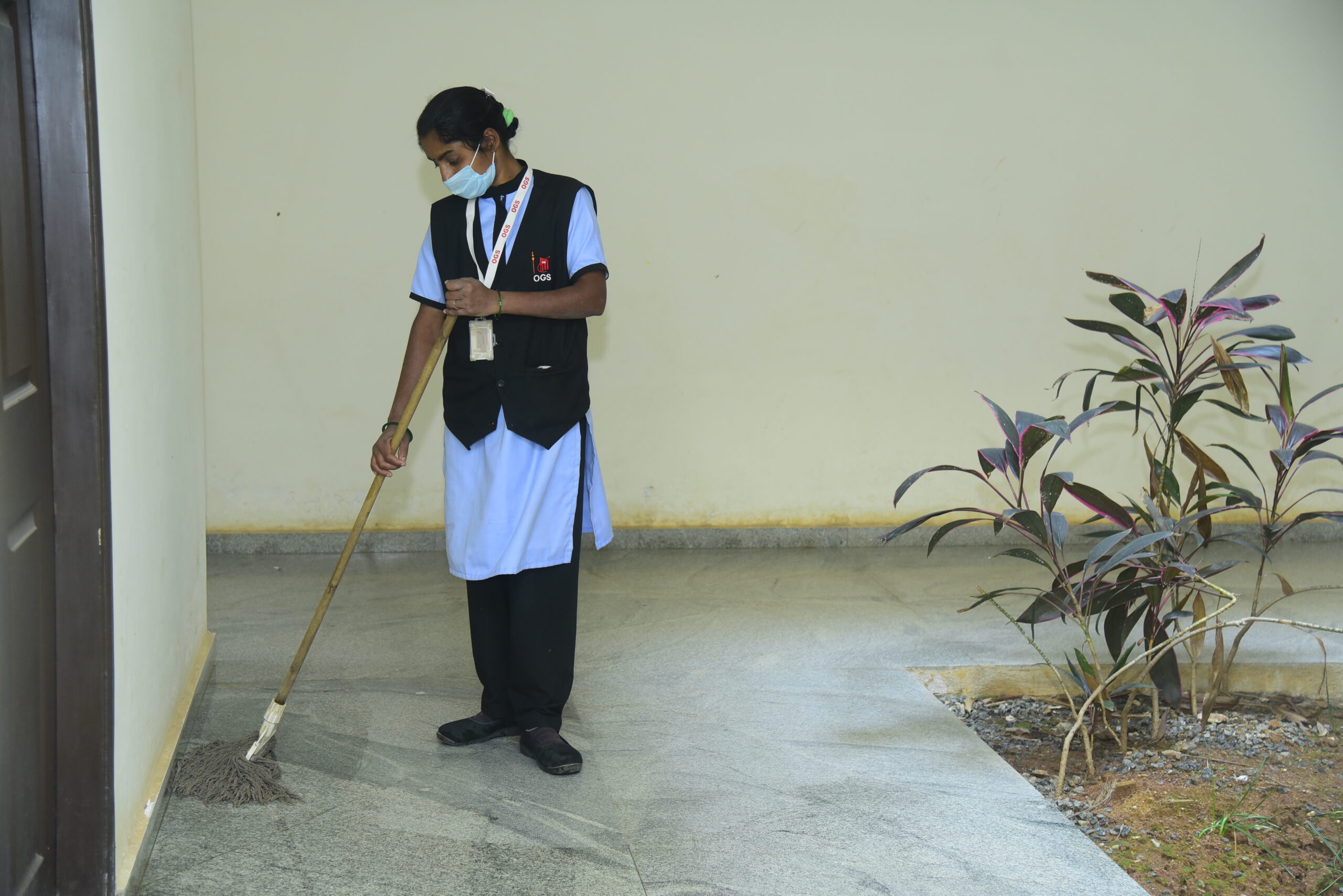A staff member in uniform mops a building corridor near indoor plants, representing Soft Services in Bangalore