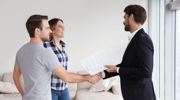 Smiling couple meeting with a professional in a suit, shaking hands while holding documents, symbolizing tenant and occupant support.